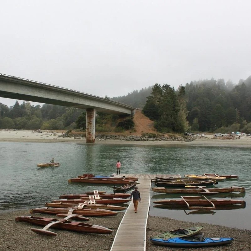 Wooden kayaks on a dock by a bridge on a foggy river